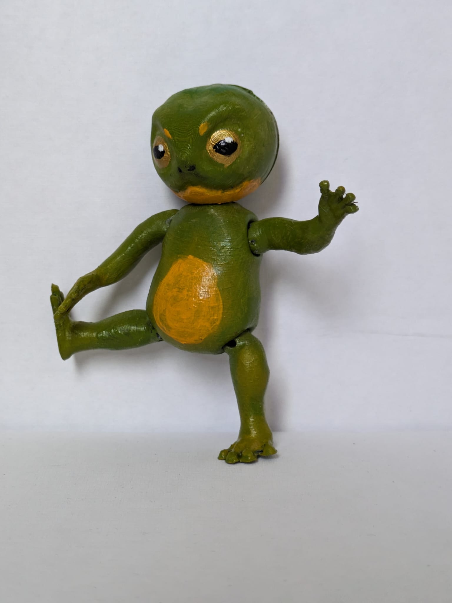 A simple bipedal frog-like doll with shoulder and hip joints. It has its right leg and left arm lifted.
