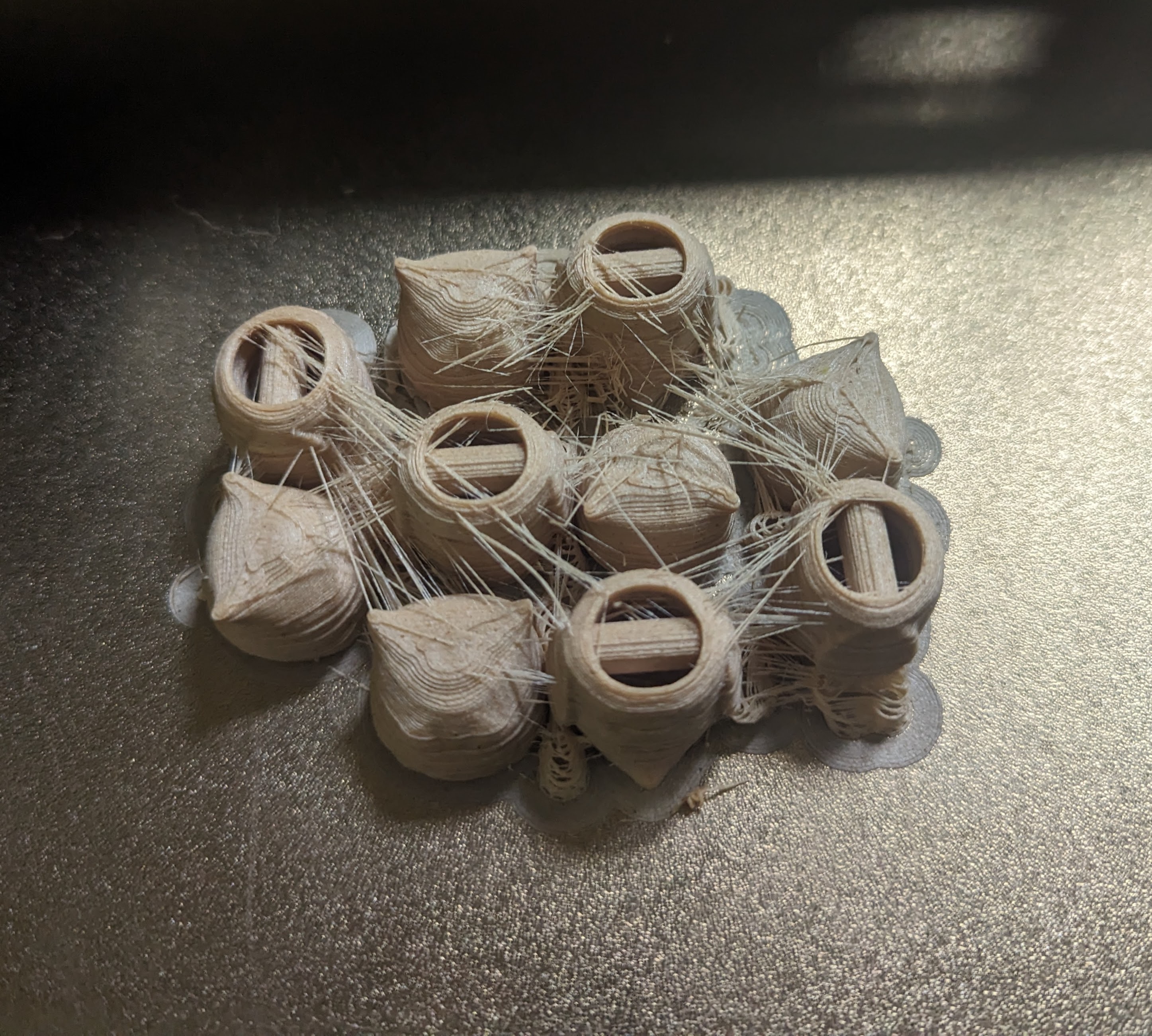 The heads and bodies of 5 3d printed owls on a 3d printer printbed. There's a web of loose 'strings' of filament between the volumes.