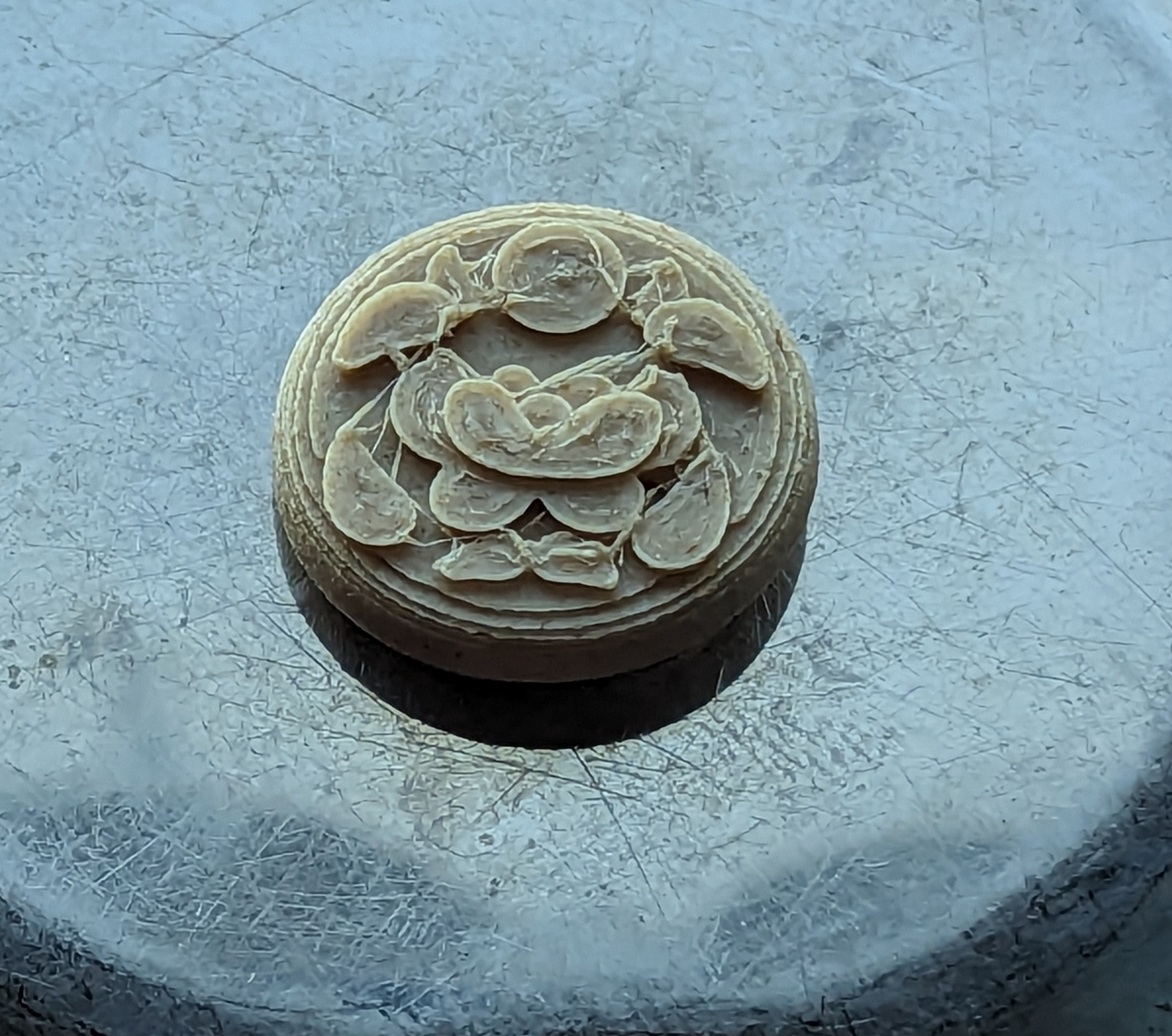 A 3d print of the previous model on a metal surface. The surface is slightly melted and uneven, and there are blobs and strings of filament between each design element.