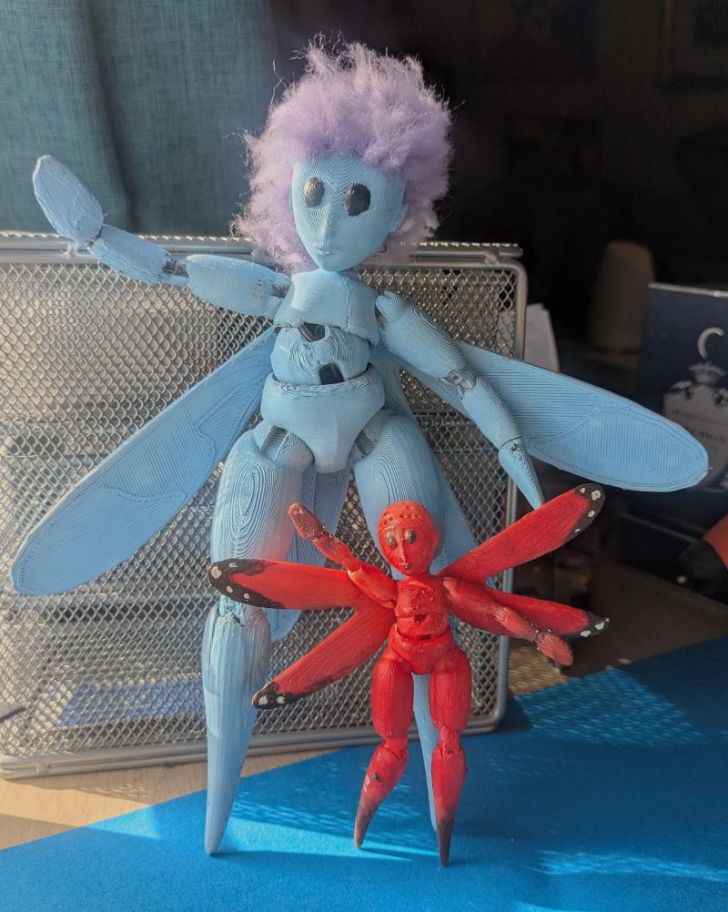 Two fairy dolls. One is larger and blue with purple hair. The other one is half as big and orange, without any hair, but painted like a monarch butterfly.