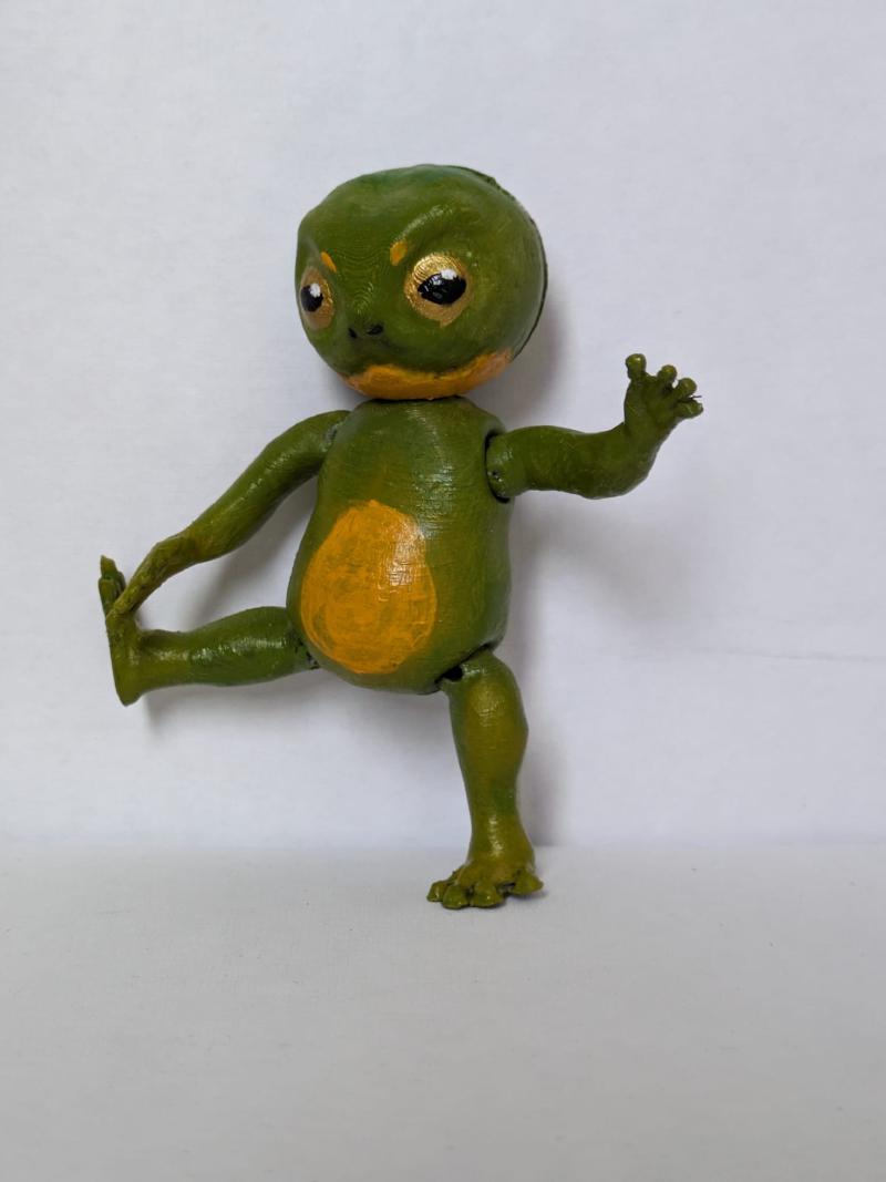 A painted frog figurine with articulated legs, arms and head on a white background. It's lifting its right leg and arm.