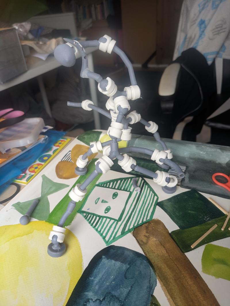 A photograph of a grey and white ball-jointed skeleton, approximately following the diagrams above, but with extra joints on the limbs. It's standing on an abstractly patterned tea-tray.