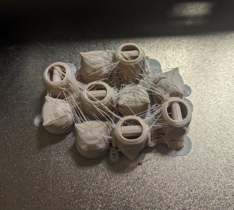 The heads and bodies of 5 3d printed owls on a 3d printer printbed. There's a web of loose 'strings' of filament between the volumes.